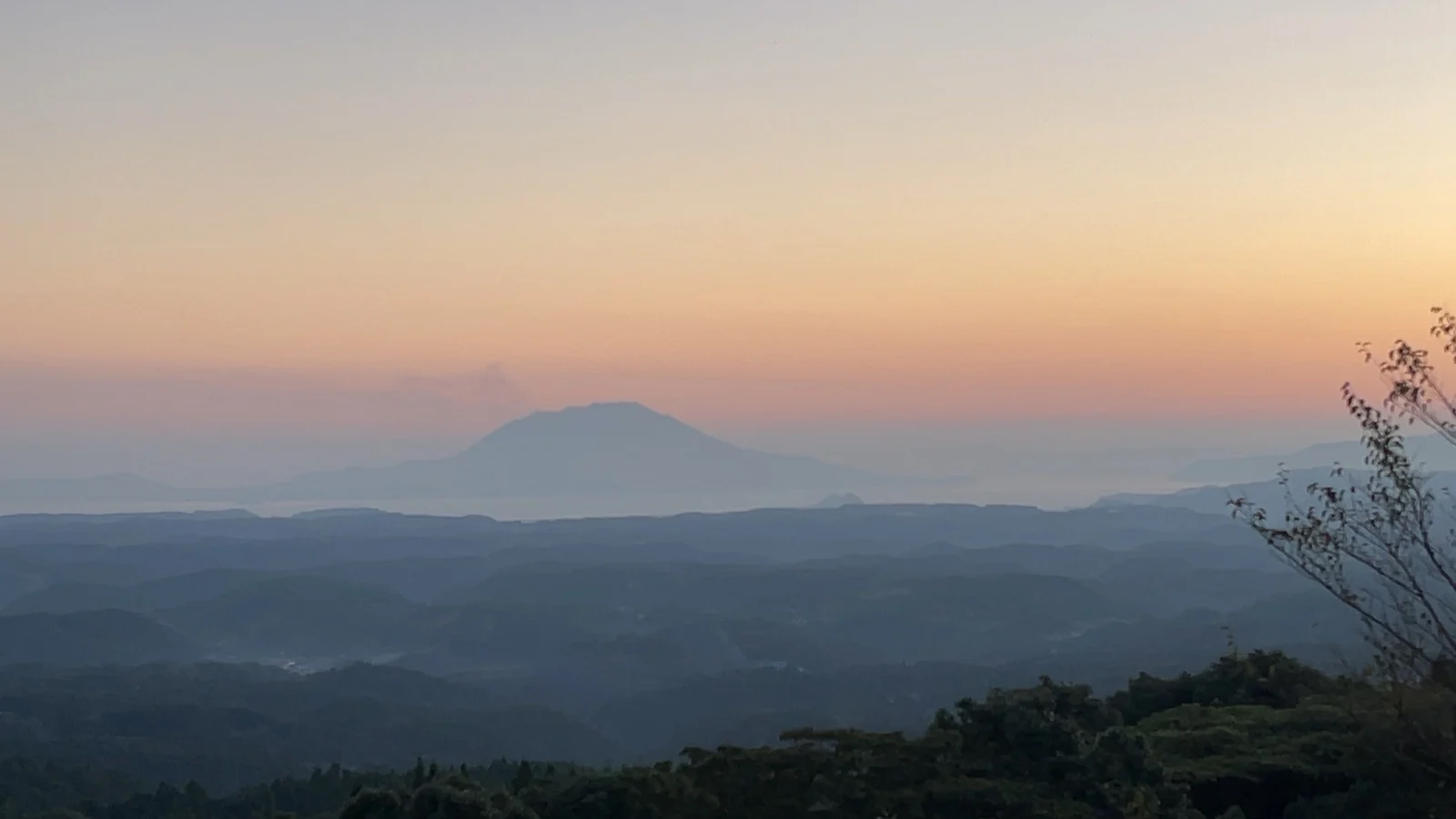 夕焼けの空に浮かぶ桜島。手前は幾重にも重なる山なみ